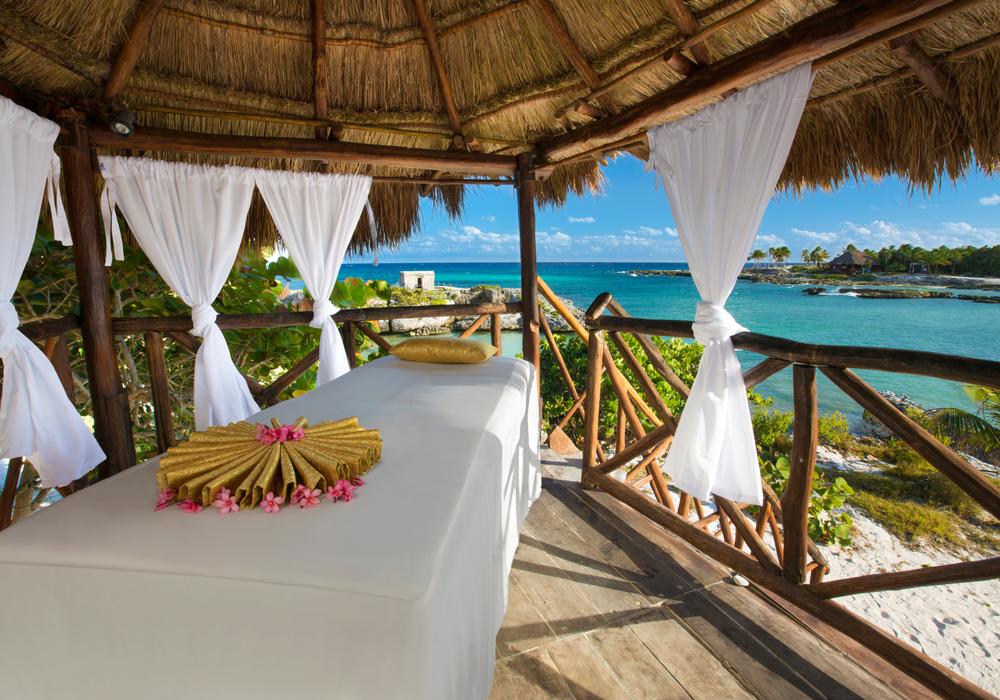 Beachfront massage gazebo with ocean view, white curtains, and flower decoration.